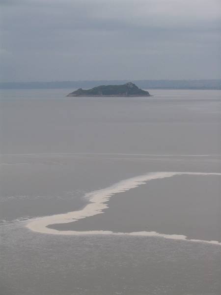 Rocky island in grey sea, white foam on choppy water