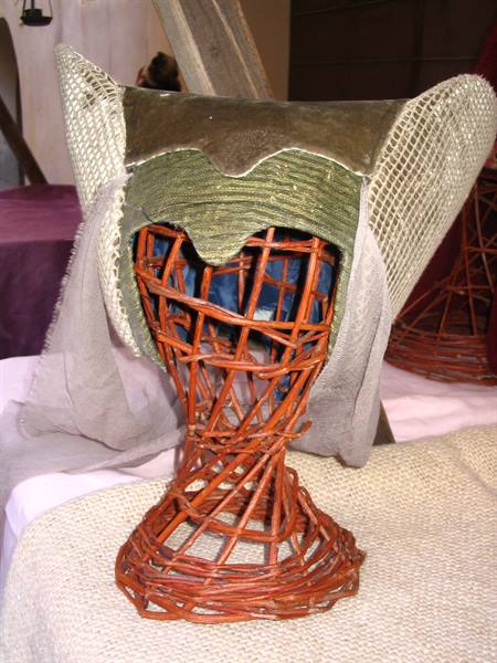 Medieval green fabric hat displayed on a woven wicker stand