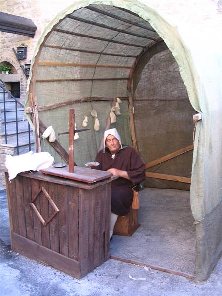 Man in medieval costume works under a canvas tent with wooden counter