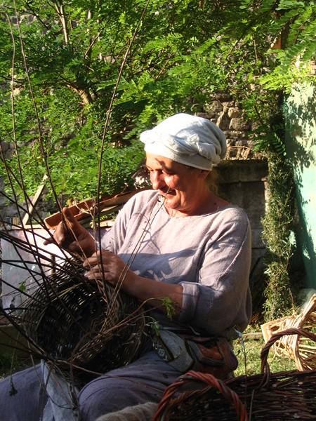 Woman in white headwrap weaving wicker baskets in the shade of trees