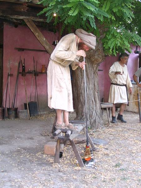 Craftsman in medieval costume blows glowing glass under a tree