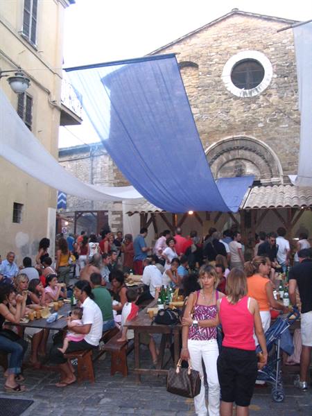 Street feast with crowded tables and blue cloths before the stone church