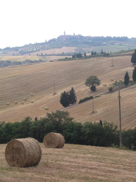 Hay bales in plowed fields, hills and hilltop village with tower behind