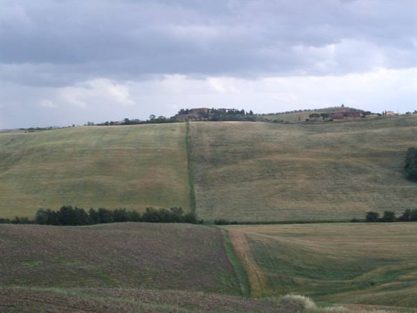 Plowed hills under cloudy sky, farmhouse on the ridge