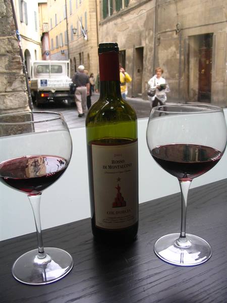 Bottle of Rosso di Montalcino with two wine glasses, medieval street behind