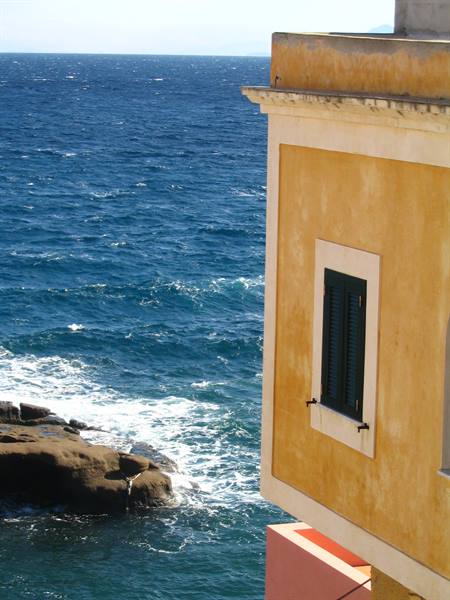 Ochre house with green shutters above the blue waves