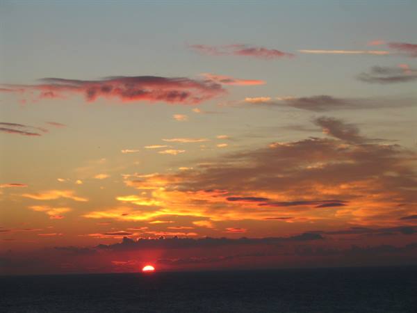 Red sun sinking over the sea horizon, orange clouds glowing in the sky