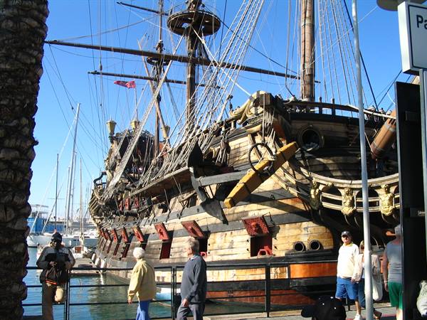 Tourists walk beside the wooden galleon Neptune moored at Genoa harbor