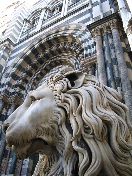 Marble lion in front of the black and white striped facade of Genoa Cathedral