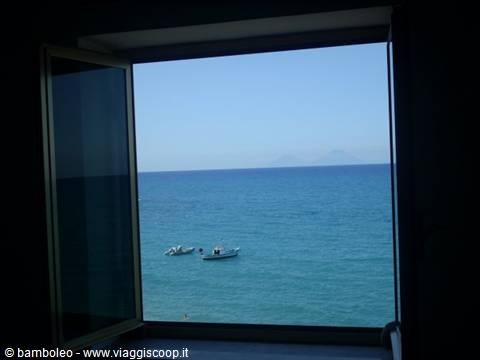 White boat on turquoise sea seen through an open dark window