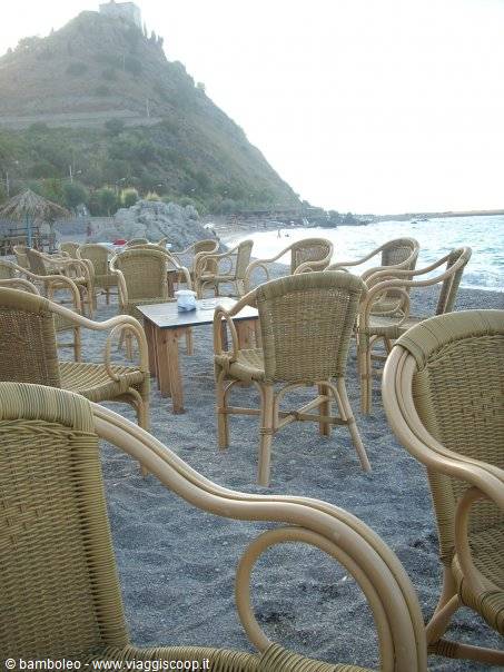 Wicker chairs on pebble beach, hilltop castle, soft evening light