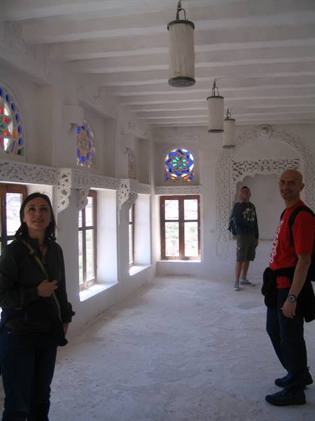 Tourists in a white plastered hall with colorful stained glass windows and hanging lanterns