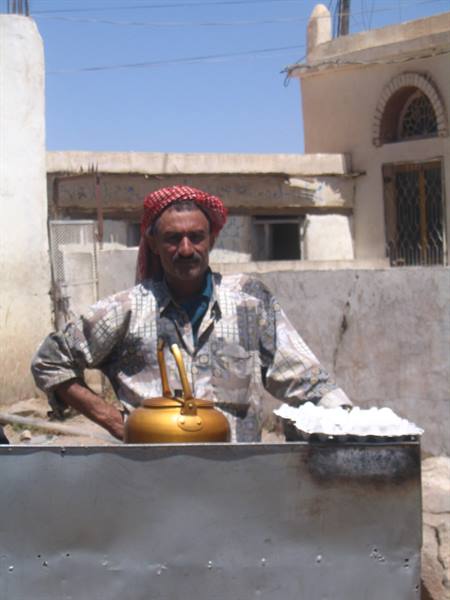 Man in red headscarf beside a golden kettle in a village