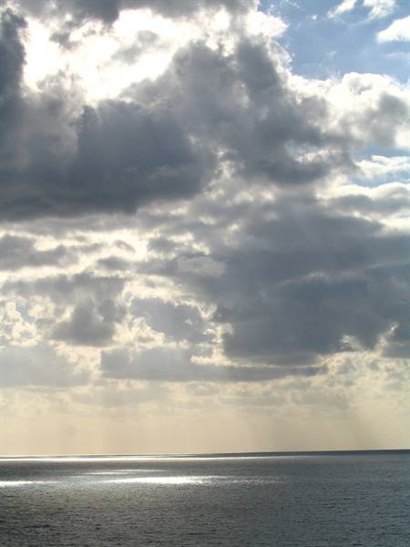 Bright clouds over calm sea, sunbeams filter through and reflect on the water