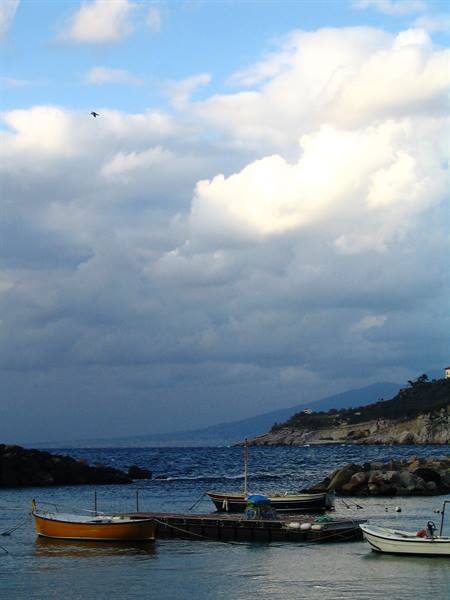 Wooden boats moored at the pier under puffy clouds, rocky coastline behind