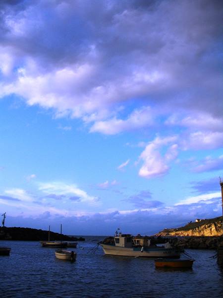 Fishing boats moored in the harbour beneath blue evening clouds