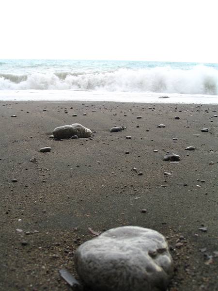 Smooth stones on dark sand beach, white waves crashing on the sea