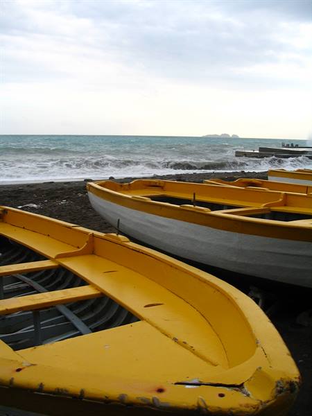 Yellow wooden fishing boats ashore on black sand, waves and cloudy sky