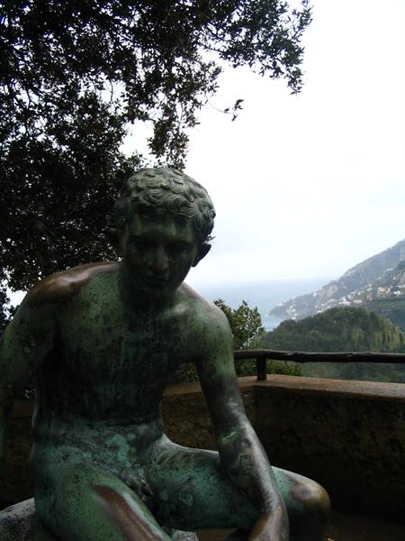 Green bronze seated statue, trees and coastline with sea behind