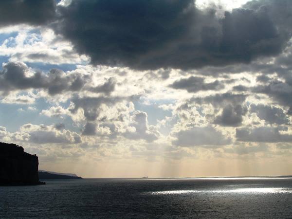 Cliffs at left over the sea, sunbeams break through dark clouds