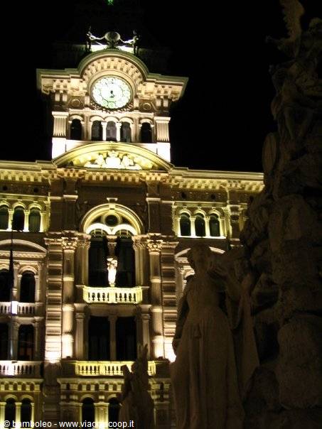 Trieste Town Hall lit at night with clock and fountain statues