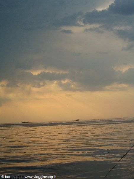 Distant ships on calm sea under grey clouds and golden light