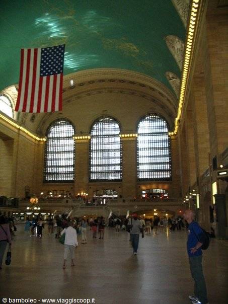 American flag hanging under the green ceiling of Grand Central Terminal, travelers walking
