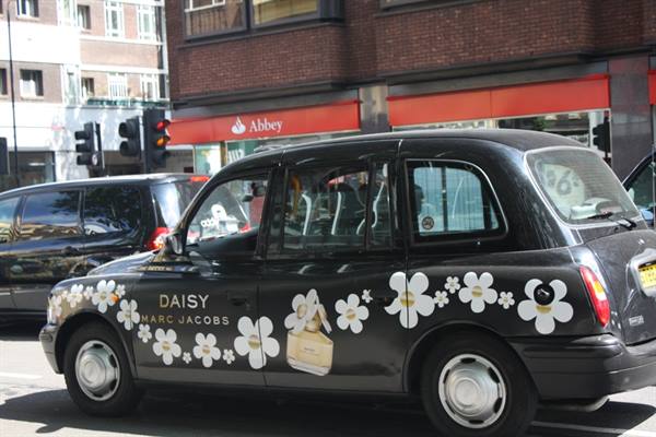 Black London taxi with Marc Jacobs flower ads outside shops