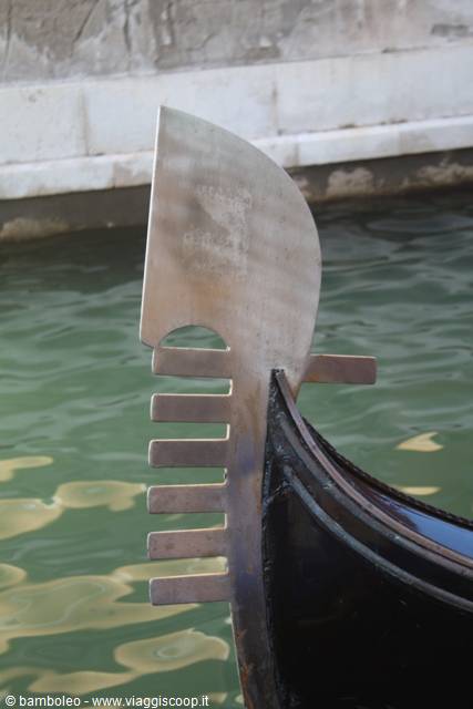The iron prow of a black gondola on green water in Venice