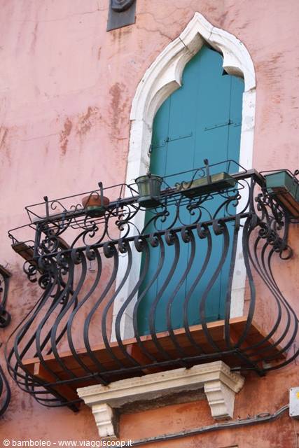 Wrought iron balcony before a green Gothic doorway on pink facade, Venice