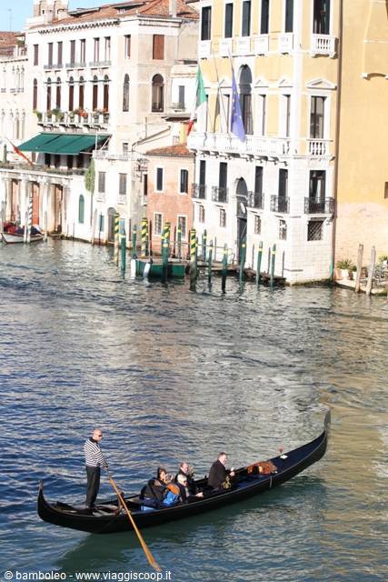 Gondolier with passengers on the Grand Canal, historic palaces and mooring poles in Venice