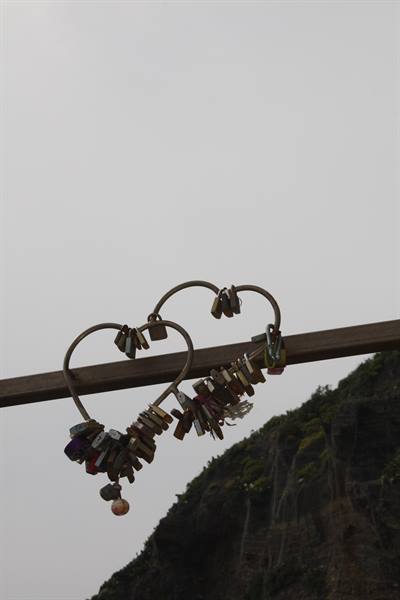 Heart-shaped love padlocks hanging on a metal bar against grey sky