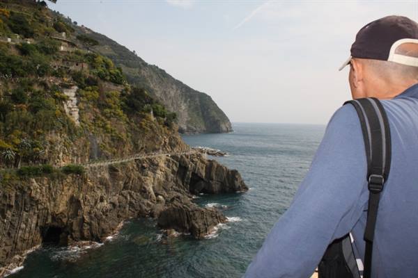 Man in cap and backpack gazes at rocky cliffs and coastal path above the sea
