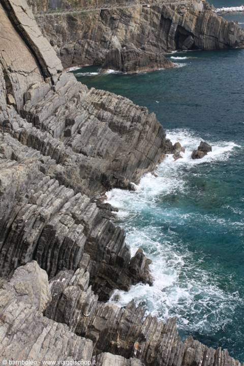 Layered rocky cliffs plunging into turquoise sea, waves crashing below