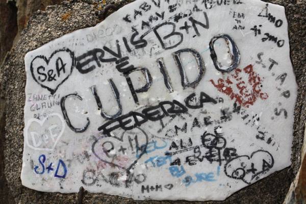 White metal plaque covered with lovers' names, hearts and graffiti, including Cupido