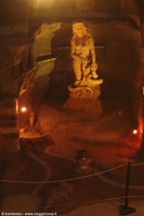 Female statue carved into rock, lit by warm light in underground cave