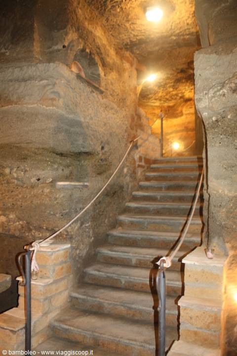 Stone staircase carved in tuff with rope handrail under warm lamps