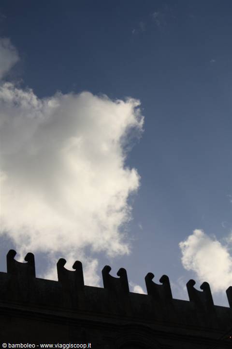 Stone battlements silhouetted against white clouds and blue sky