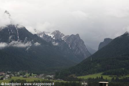 Snowy Dolomite peaks wrapped in clouds above a village on green meadows
