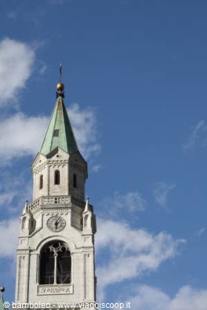 White stone bell tower with green copper spire against blue sky