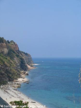 Beach beneath green rocky cliffs, blue sea ahead