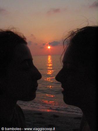 Two silhouetted profiles face each other, red sun setting over the sea