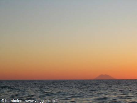 Stromboli volcano rising from the sea at dusk, orange sky over dark water