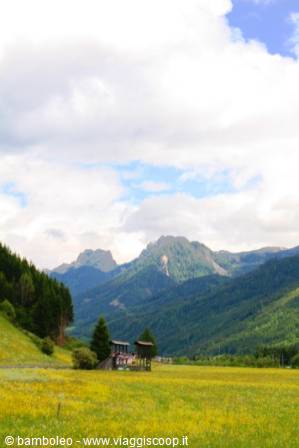 Wooden chalet on green meadow beneath the Dolomites, cloudy sky
