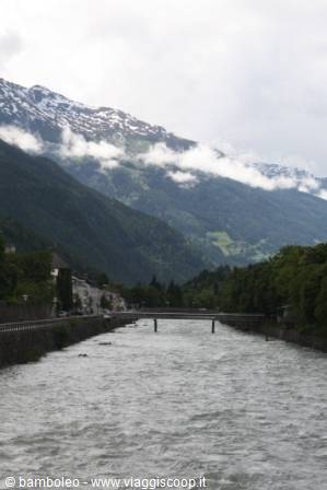 Bridge over the Adige river among snowy mountains and clouds