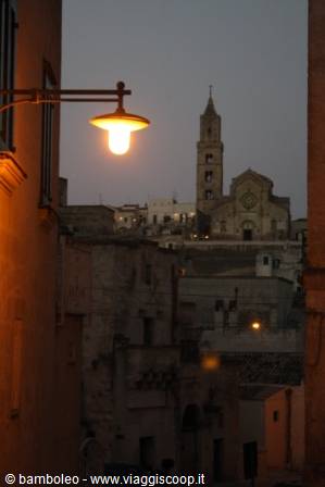 Lit street lamp over old tufa buildings, Matera Cathedral in dusk