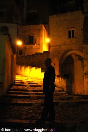 Man silhouetted on illuminated stone stairs, alley in Matera's Sassi