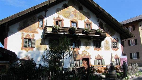 Frescoed Bavarian house with wooden balcony, flower boxes, blue sky