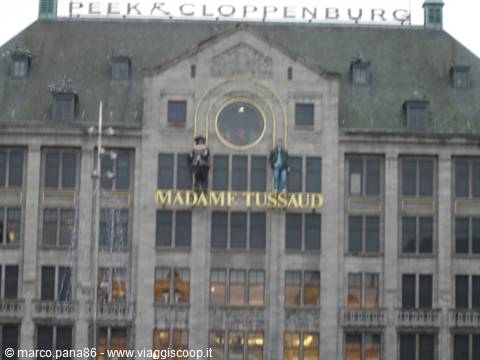 Grey facade of Madame Tussauds and Peek & Cloppenburg, figures hanging under soft daylight