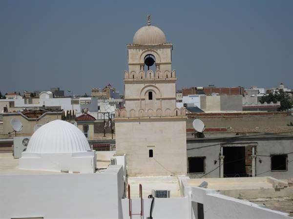 Stone minaret with dome rising above whitewashed medina rooftops in sunlight